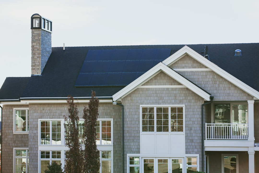 Ein zweistöckiges Haus mit grauem Schindelverkleidung, großen Fenstern und Solarpaneelen auf dem Dach.